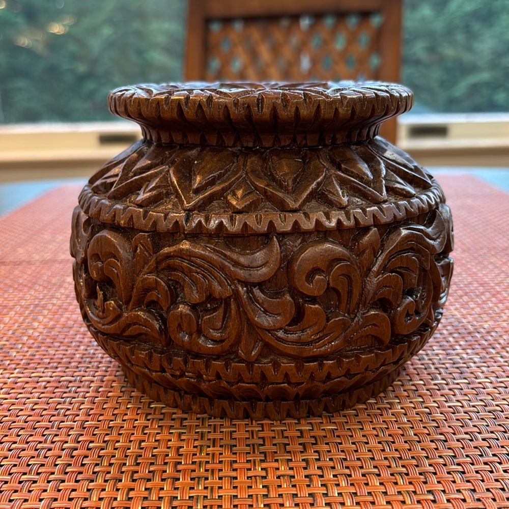Hand carved and turned decorative wooden vase with round shape and curved lip.